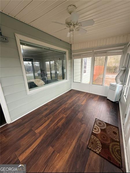 unfurnished sunroom featuring a ceiling fan and a wall mounted AC