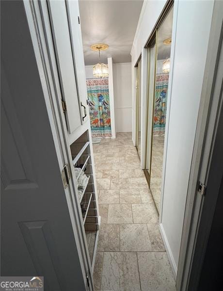 hall featuring an inviting chandelier, baseboards, and stone finish floor