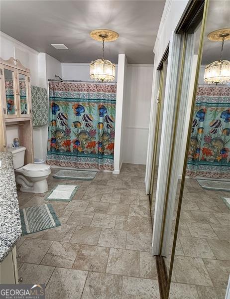 bathroom featuring curtained shower, toilet, stone finish floor, vanity, and a chandelier