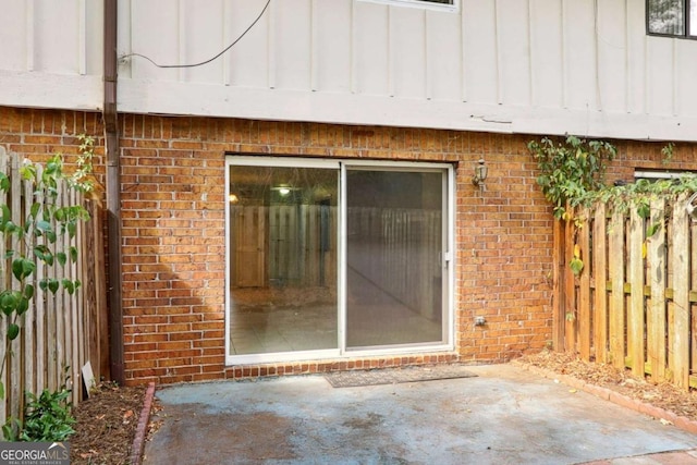 entrance to property featuring a patio, brick siding, board and batten siding, and fence