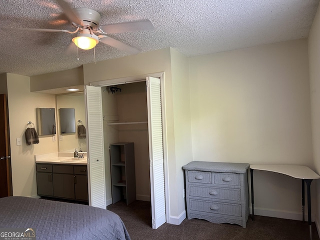 bedroom with a textured ceiling, a closet, dark colored carpet, and a sink