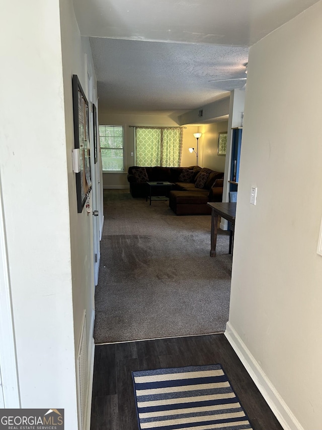 hallway featuring dark colored carpet, dark wood-style flooring, and baseboards