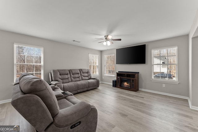 living area featuring a lit fireplace, visible vents, light wood-style flooring, and a wealth of natural light