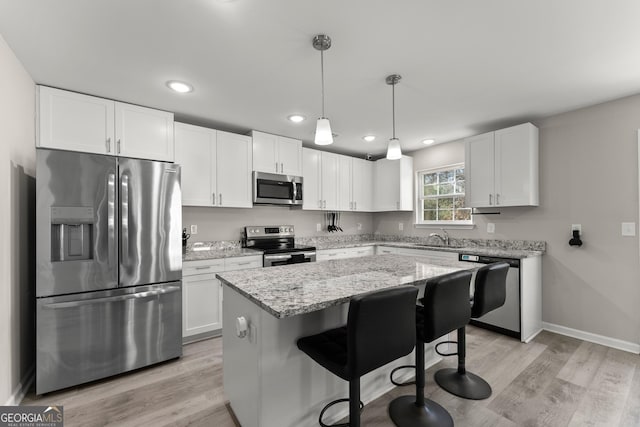 kitchen featuring a kitchen island, white cabinetry, hanging light fixtures, appliances with stainless steel finishes, and light stone countertops