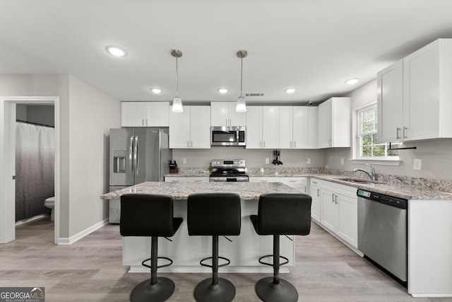 kitchen with a center island, pendant lighting, stainless steel appliances, white cabinets, and a sink