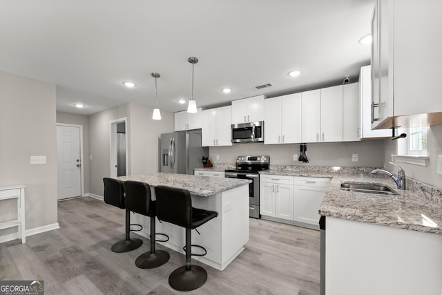 kitchen featuring white cabinets, appliances with stainless steel finishes, a center island, hanging light fixtures, and a sink