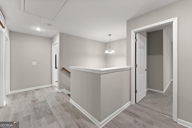 hall featuring light wood-style floors, attic access, baseboards, and an upstairs landing