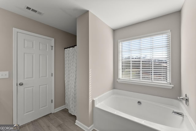 bathroom with a garden tub, baseboards, visible vents, and wood finished floors