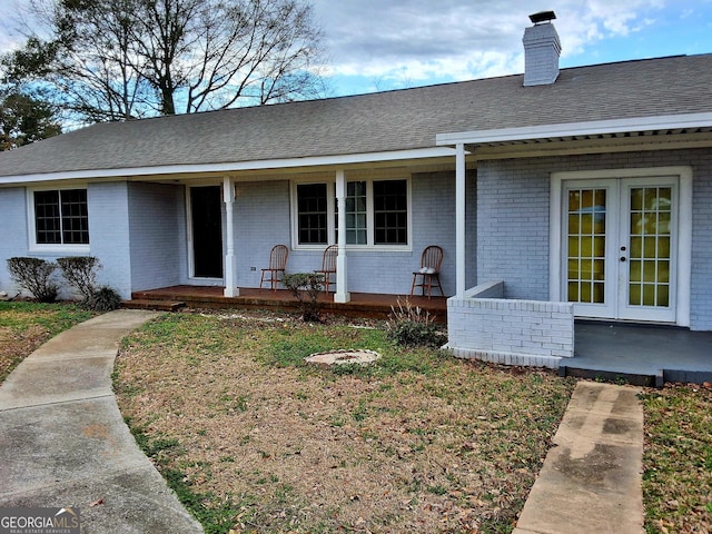 view of front of property with roof with shingles, covered porch, a chimney, french doors, and brick siding