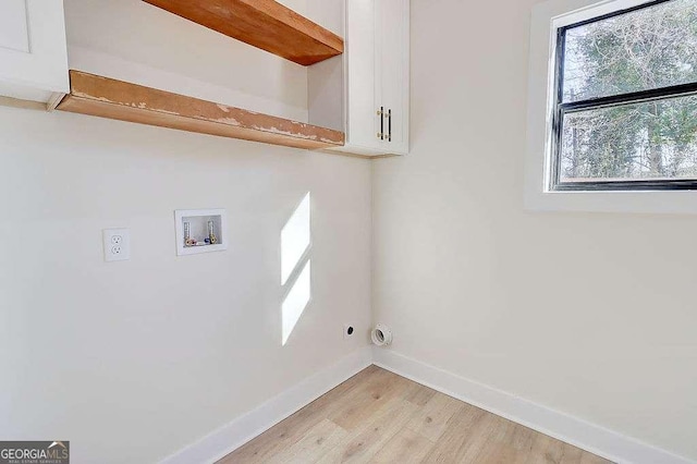 washroom with hookup for a washing machine, cabinet space, light wood finished floors, and baseboards