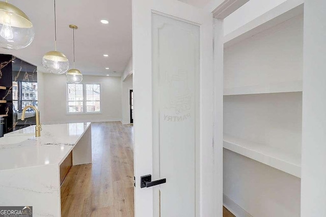 interior space featuring light wood finished floors, light stone counters, pendant lighting, a sink, and recessed lighting