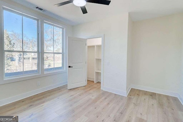 unfurnished bedroom featuring light wood-type flooring, baseboards, visible vents, and a walk in closet