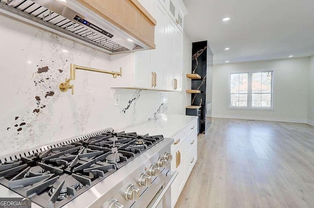 kitchen with custom exhaust hood, glass insert cabinets, white cabinets, stainless steel range with gas stovetop, and light stone countertops