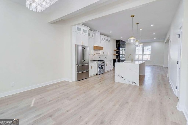 kitchen featuring hanging light fixtures, premium appliances, a center island with sink, and white cabinetry