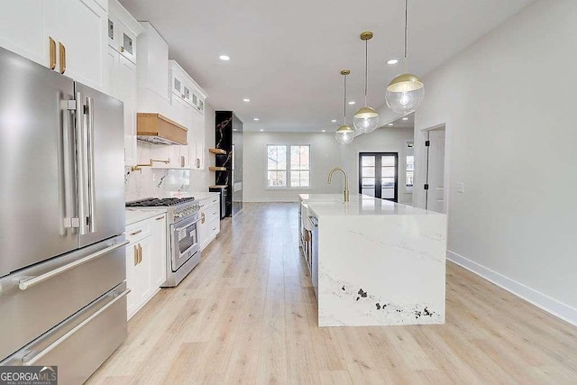 kitchen with a center island with sink, high quality appliances, glass insert cabinets, white cabinetry, and pendant lighting