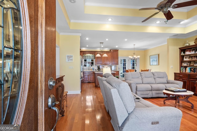 living room with light wood-style floors, a tray ceiling, and crown molding