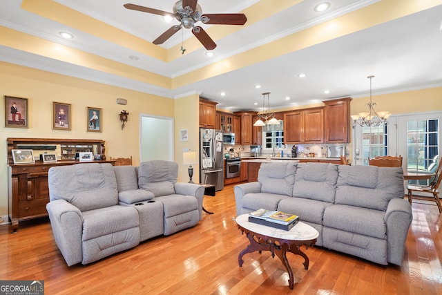 living area featuring a tray ceiling, recessed lighting, light wood-style floors, ornamental molding, and ceiling fan with notable chandelier