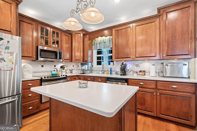 kitchen featuring hanging light fixtures, appliances with stainless steel finishes, light countertops, a center island, and glass insert cabinets