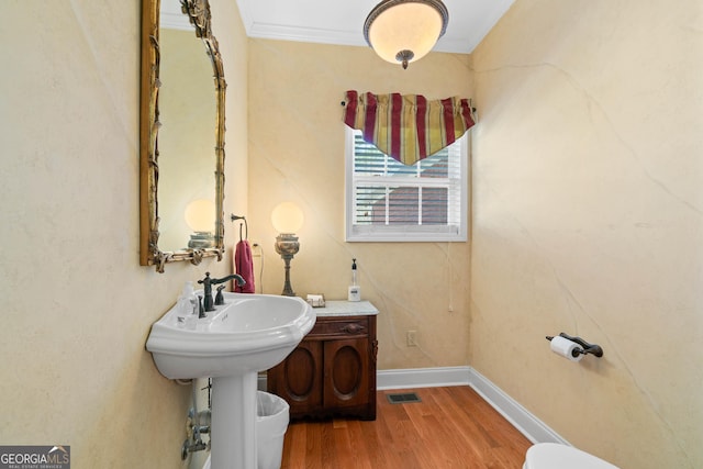 bathroom with ornamental molding, wood finished floors, visible vents, and baseboards