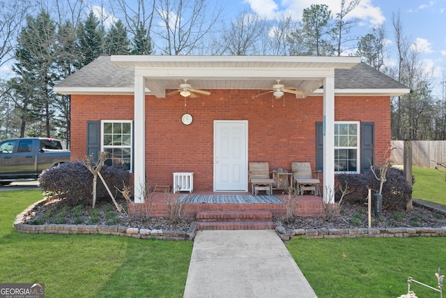 property entrance featuring a yard, brick siding, ceiling fan, and fence