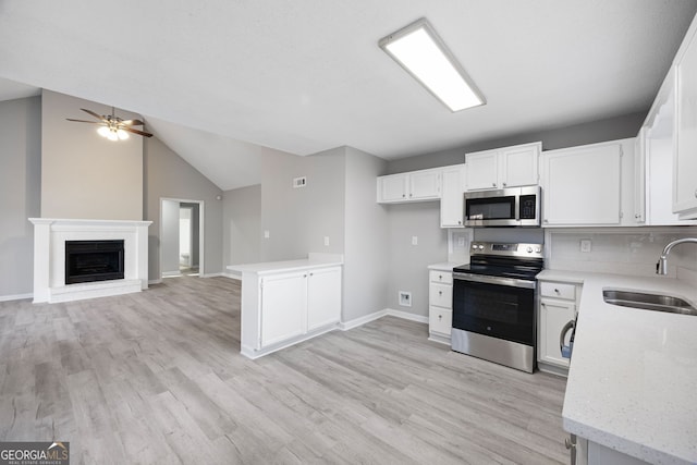 kitchen featuring stainless steel appliances, light wood-style flooring, open floor plan, white cabinetry, and a sink