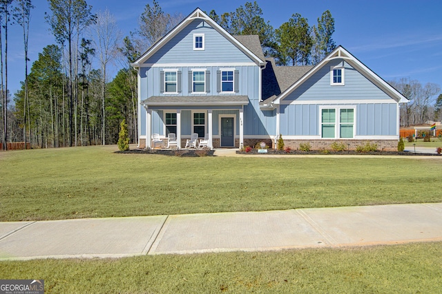 view of front of house with a shingled roof, covered porch, a front lawn, board and batten siding, and brick siding