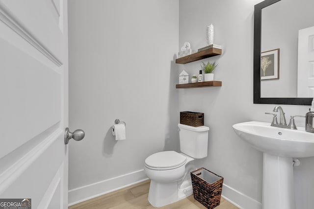 half bath with a sink, wood finished floors, toilet, and baseboards