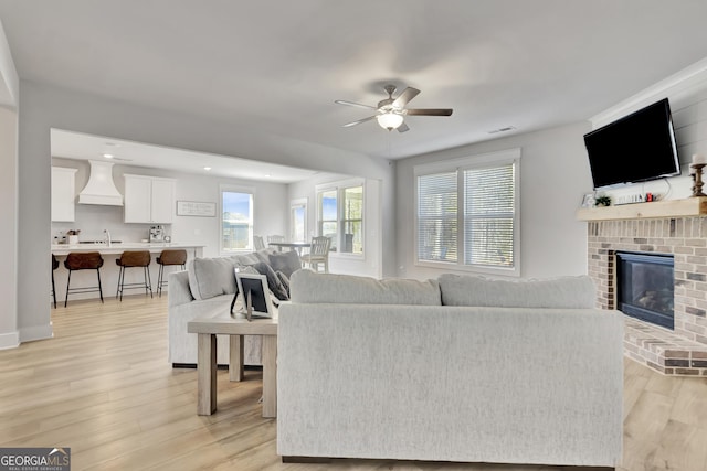 living area featuring visible vents, light wood finished floors, a fireplace, and a ceiling fan