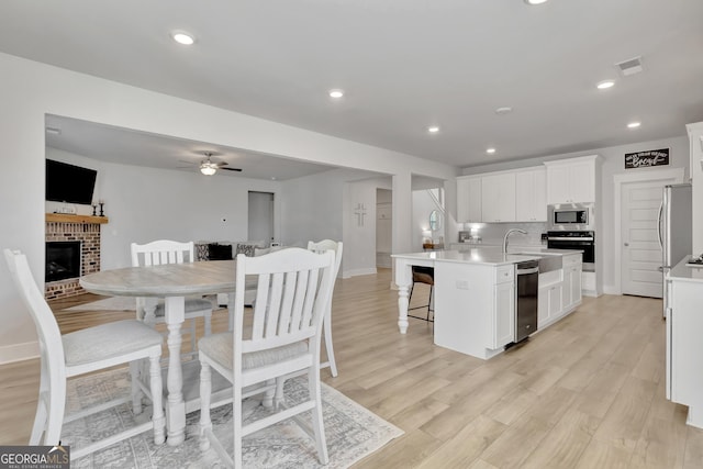 kitchen with a center island with sink, white cabinets, open floor plan, stainless steel appliances, and light countertops