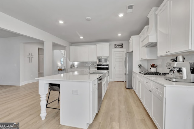 kitchen with light countertops, appliances with stainless steel finishes, a kitchen island with sink, and white cabinetry