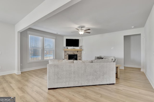 living room with light wood-style floors, a brick fireplace, baseboards, and a ceiling fan