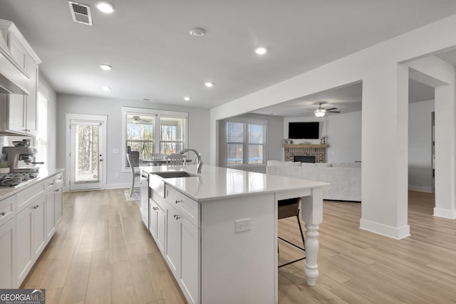 kitchen featuring a sink, white cabinetry, light countertops, an island with sink, and stainless steel gas stovetop