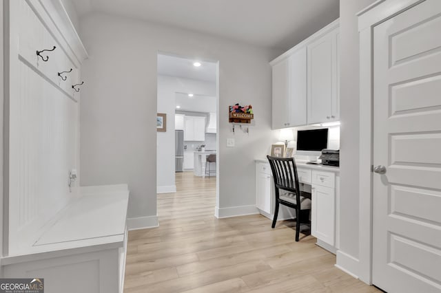 office area with light wood-style floors, built in desk, and baseboards