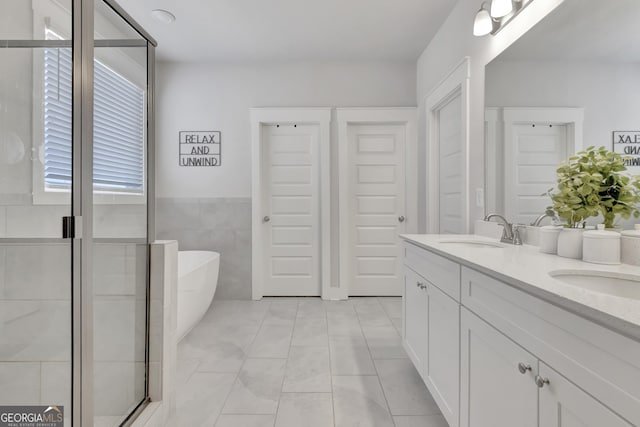 full bathroom with double vanity, a freestanding bath, tile walls, and a sink