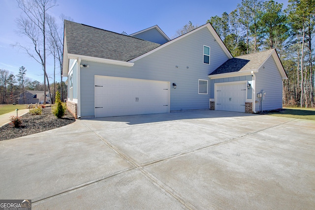 view of side of home with concrete driveway, a shingled roof, board and batten siding, and an attached garage