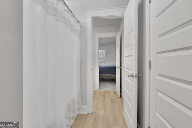 hallway featuring light wood-style floors, visible vents, and baseboards