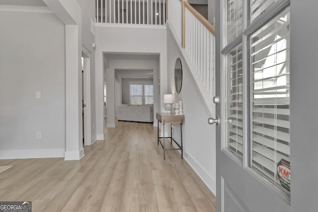 foyer with light wood-type flooring, a towering ceiling, and baseboards