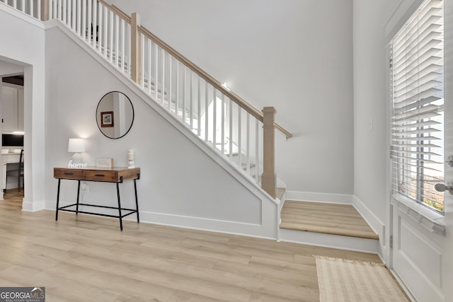 stairway featuring a towering ceiling, baseboards, and wood finished floors