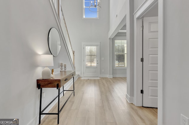 entryway featuring a towering ceiling, light wood-style floors, baseboards, and a notable chandelier