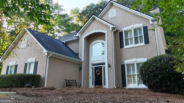 traditional home featuring roof with shingles and stucco siding