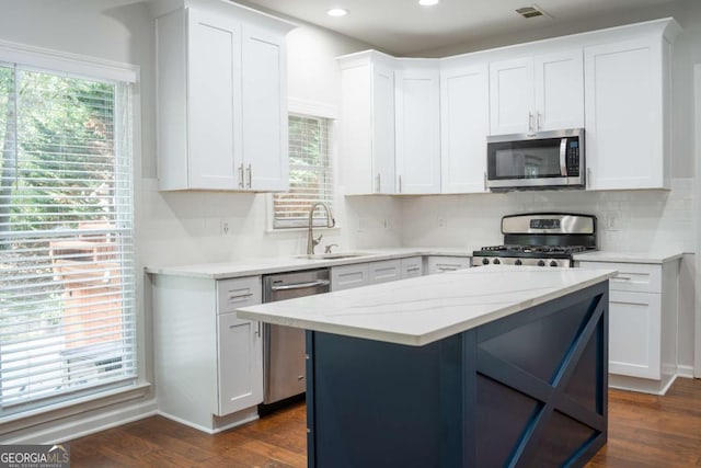 kitchen featuring a kitchen island, light stone counters, stainless steel appliances, white cabinetry, and a sink