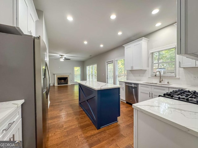 kitchen featuring appliances with stainless steel finishes, open floor plan, white cabinets, a kitchen island, and light stone countertops