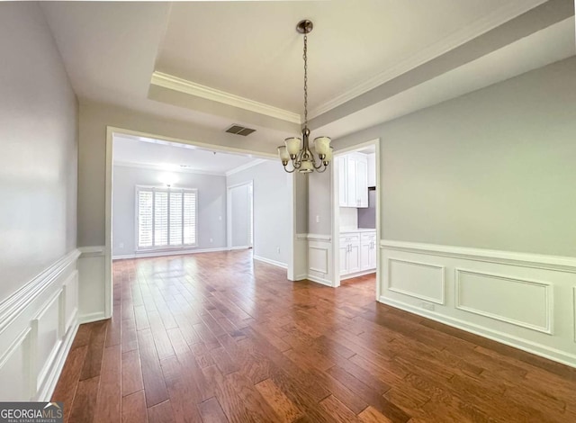 unfurnished dining area with visible vents, ornamental molding, a tray ceiling, dark wood finished floors, and an inviting chandelier