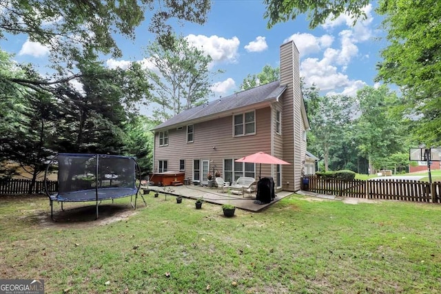 rear view of house featuring a hot tub, a chimney, a trampoline, fence, and a patio area