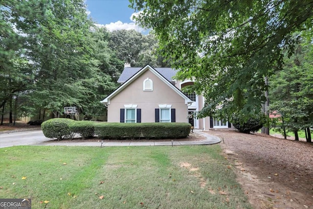 view of front of home with stucco siding, a chimney, and a front yard