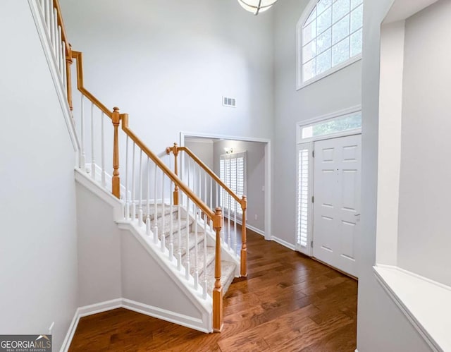 entrance foyer with visible vents, a towering ceiling, wood finished floors, baseboards, and stairs