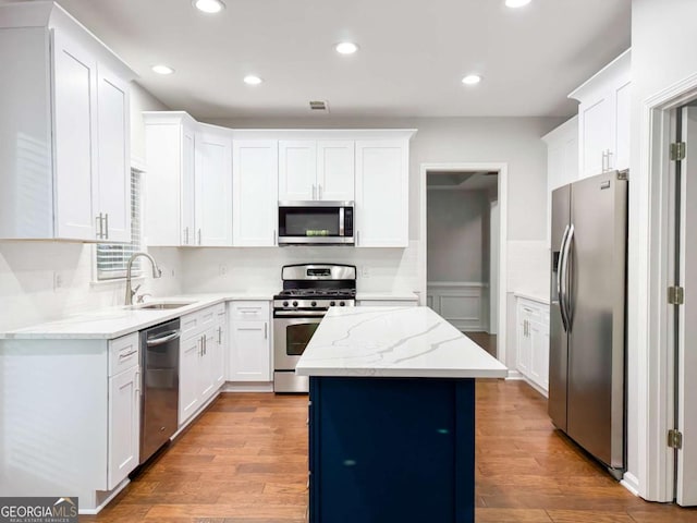 kitchen featuring stainless steel appliances, a kitchen island, a sink, white cabinets, and light stone countertops