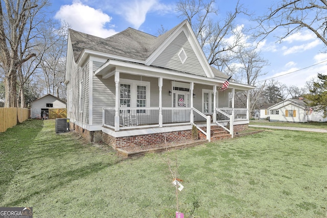 view of front of property featuring a porch, central AC, fence, roof with shingles, and a front lawn