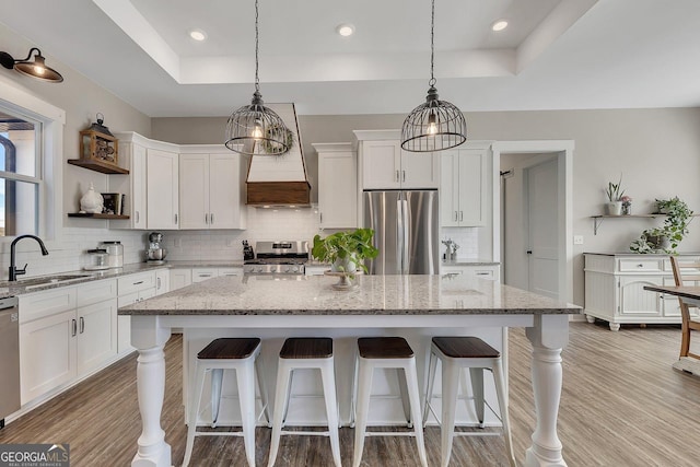 kitchen with a tray ceiling, appliances with stainless steel finishes, open shelves, and a sink