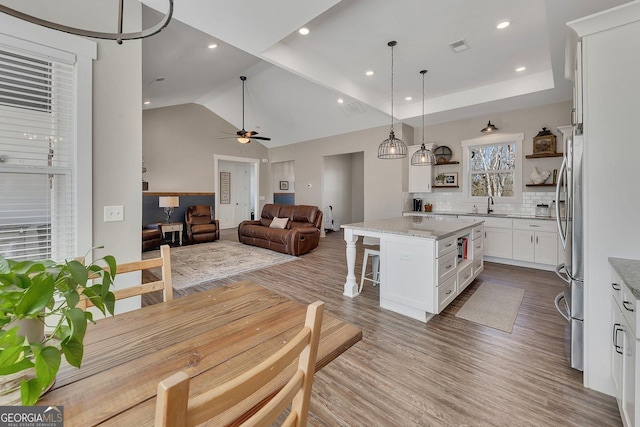 kitchen with wood finished floors, open floor plan, a center island, open shelves, and a kitchen bar